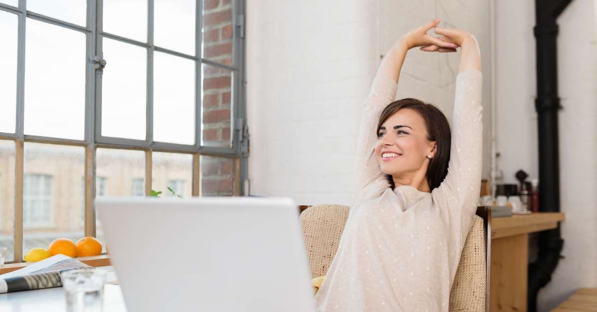 Woman looking out window, smiling and stretching at desk