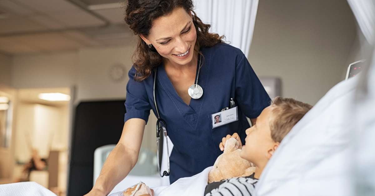 Female nurse smiling down at boy patient holding a teddy bear